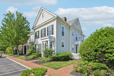 A white house with a grey roof and a brick walkway in front.