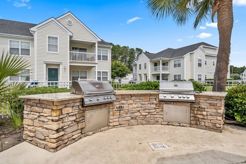 A stone wall with two built-in BBQs in front of a two-story apartment building.