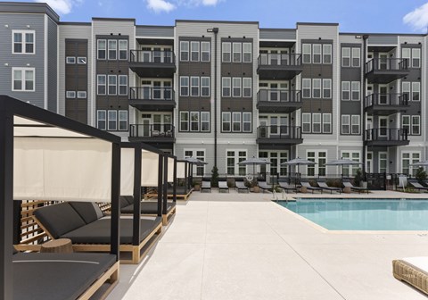 A large pool area with lounge chairs and umbrellas in front of apartment buildings.