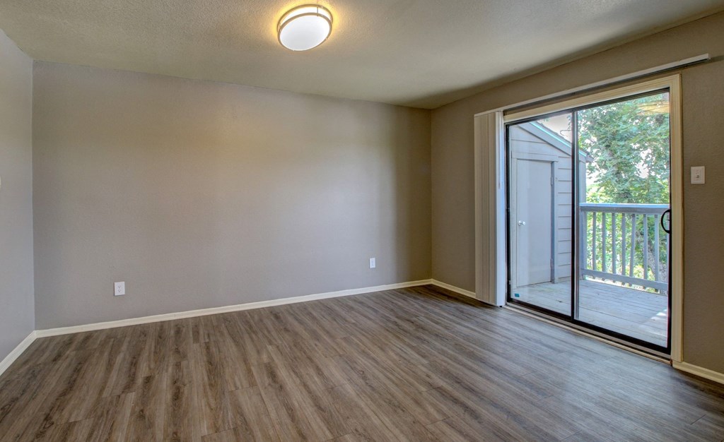 an empty living room with a sliding glass door to a balcony