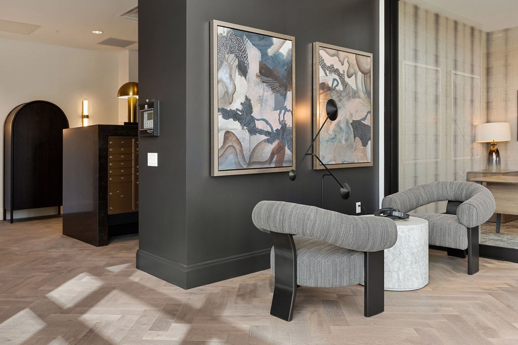 A grey couch sits in a room with a wooden floor and two paintings on the wall.