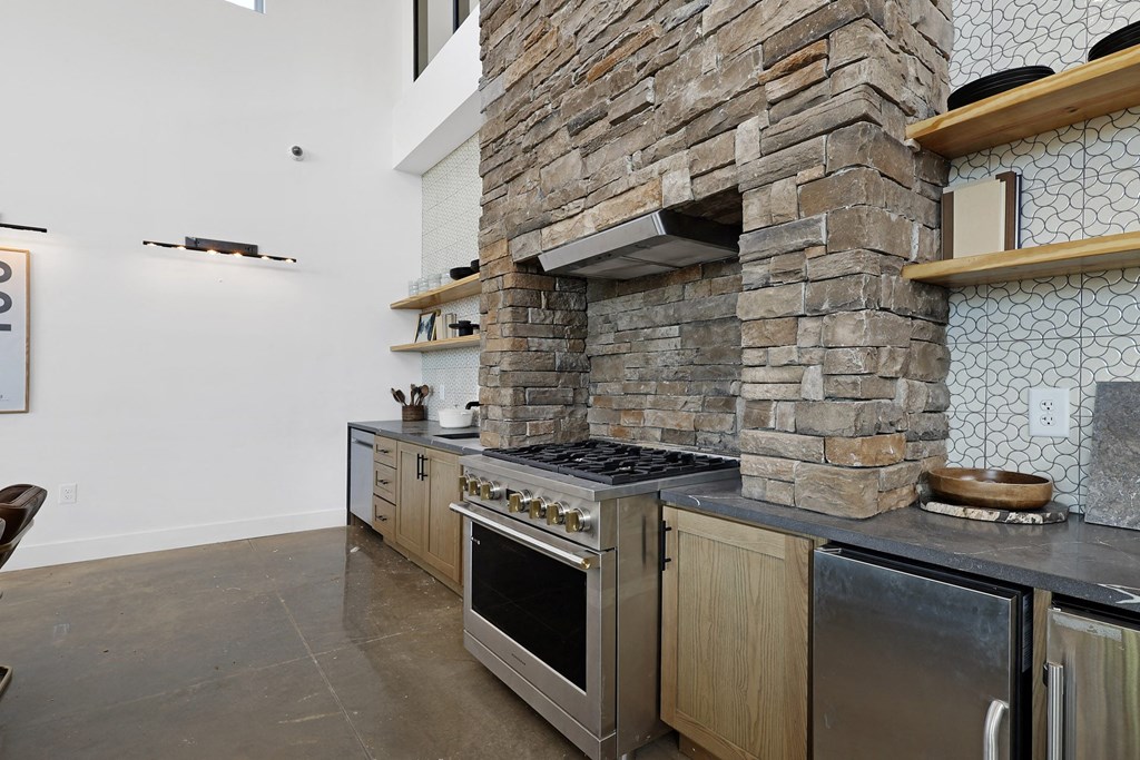A modern kitchen with a stone wall and stainless steel appliances. at Terraces at High Mountain, Huntsville