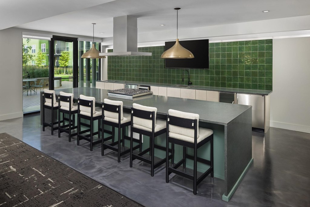 A kitchen with a green tiled backsplash and a long island with chairs.