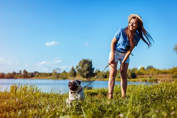 A woman is playing with her dog in a field near a lake.