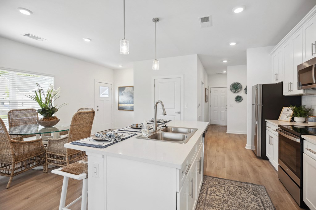 an open kitchen and dining room with white cabinets and a white island with a sink