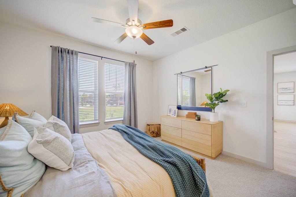 A bedroom with a bed, pillows, a blanket, a dresser, a mirror, and a ceiling fan.
