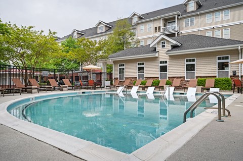A large swimming pool with lounge chairs and a building in the background.