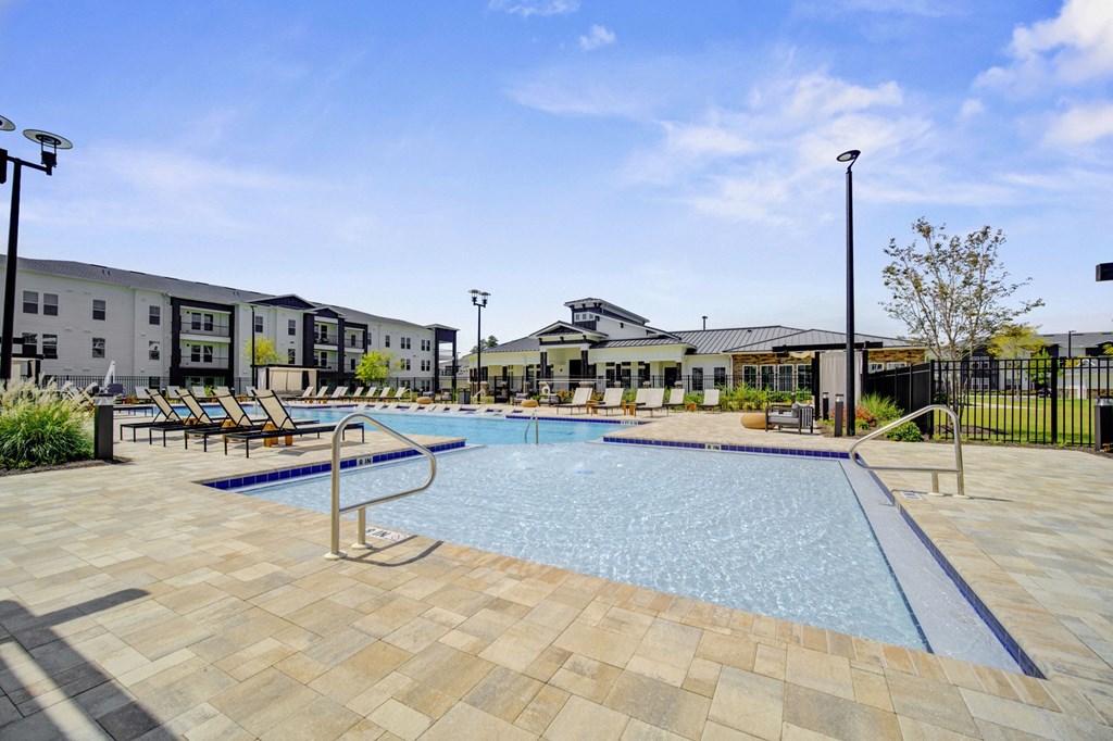 A large outdoor swimming pool surrounded by a tiled patio and lounge chairs.