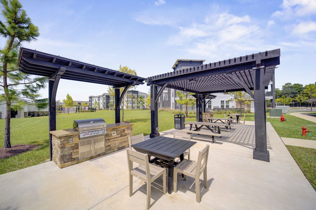 A picnic area with a grill and seating under a canopy.