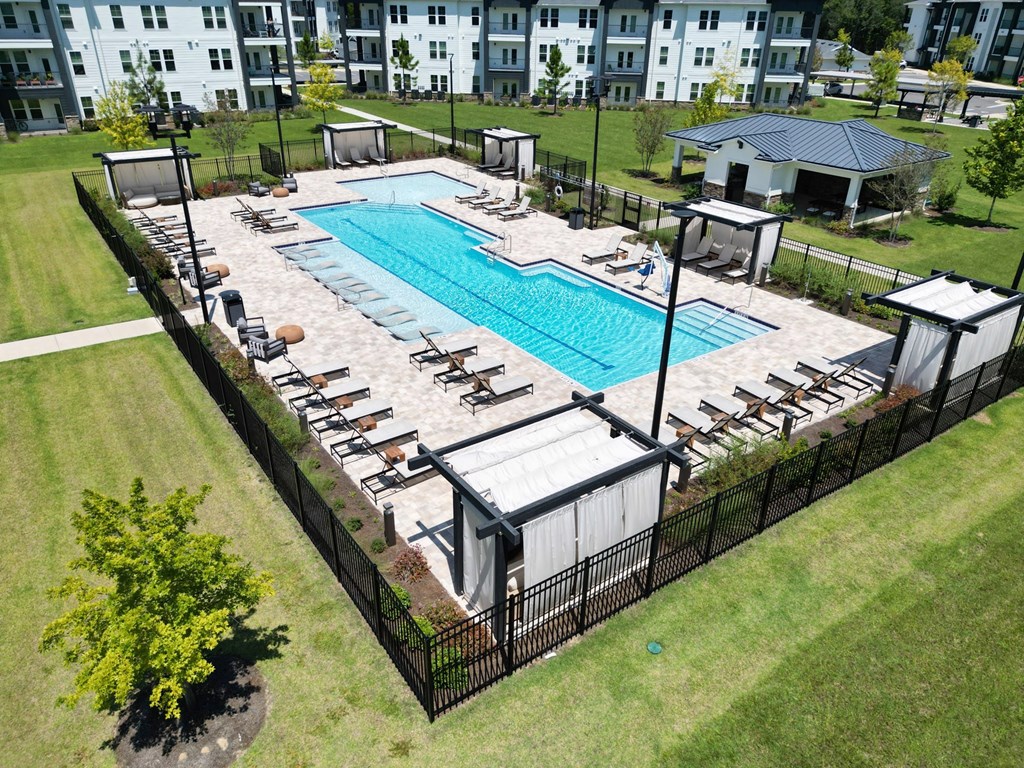 A large outdoor swimming pool surrounded by a black fence and lounge chairs.