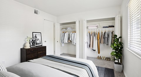 A bedroom with a bed, a dresser with a picture frame, a closet with clothes, and a potted plant.