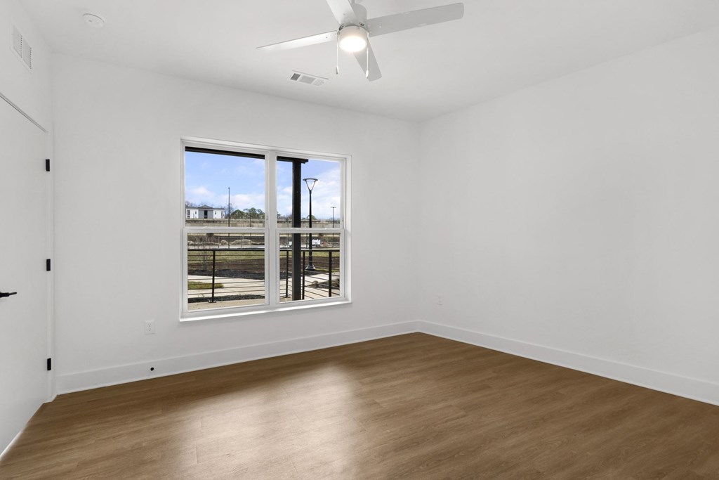 A room with a ceiling fan and a large window overlooking a parking lot.at Boardwalk at Research Park, Huntsville, AL