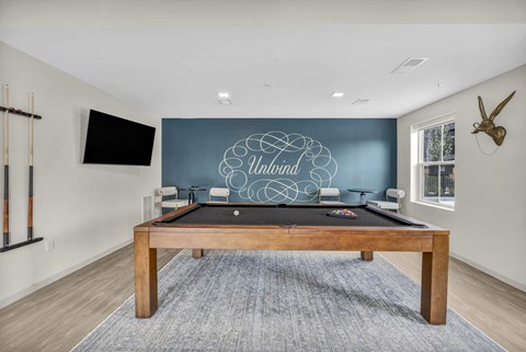 A pool table with a blue cloth and a wooden frame is in the middle of the room.