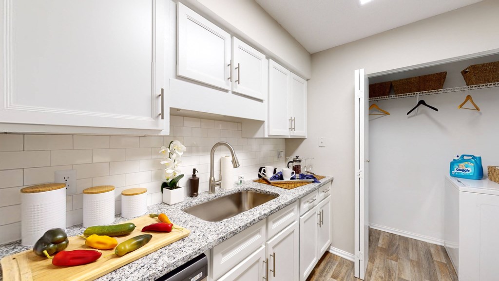 a kitchen with white cabinets and a wooden cutting board with vegetables on it