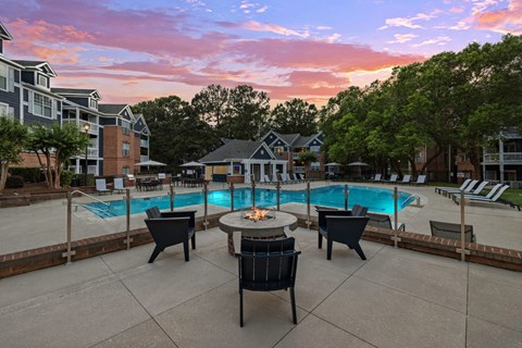 A pool surrounded by chairs and a table with a sunset in the background.