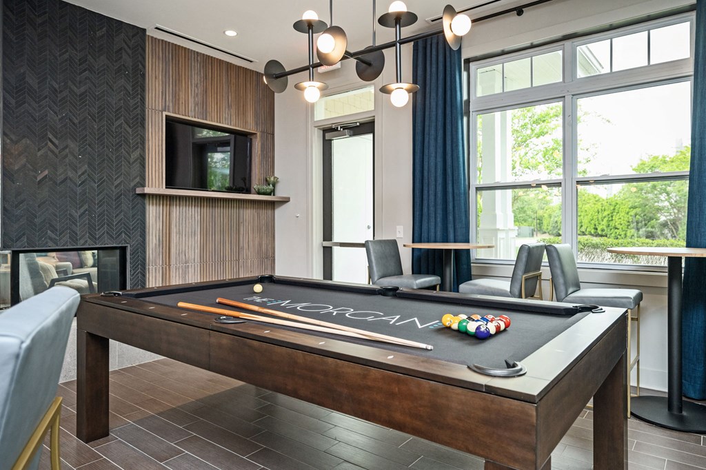 A pool table with the word "CAN" written on it in the middle of a room with a television, chair, and window.