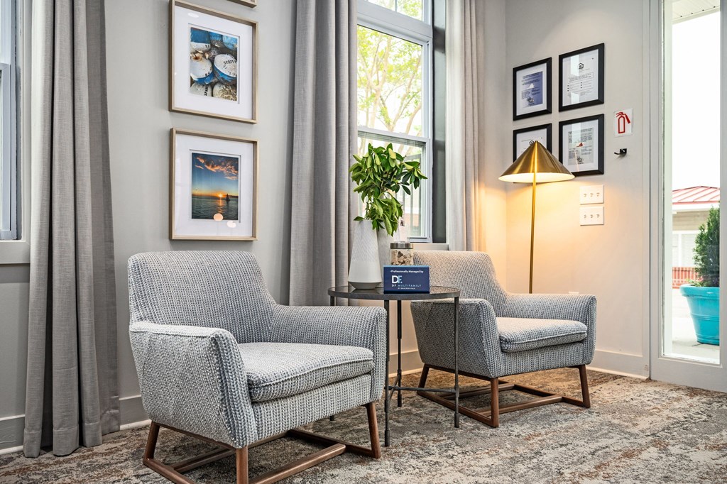 Two grey chairs are placed in a room with a table between them.