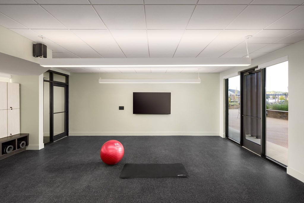 A red ball is placed on a black mat in a room with a flat screen TV mounted on the wall.