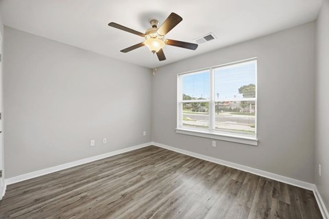 A room with a ceiling fan and a window overlooking a parking lot.