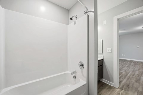 A white bathroom with a tub and a doorway leading to another room.