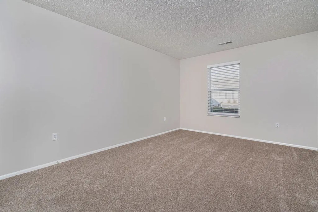 A room with a carpeted floor and a window with blinds.