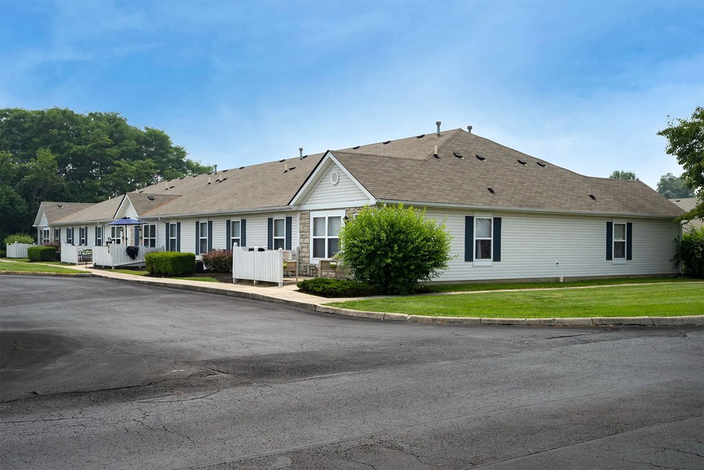 A long white building with a grey roof and a parking lot in front.