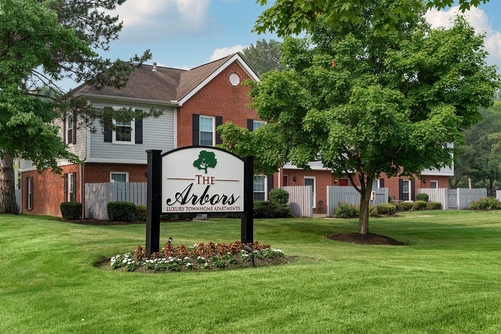 A sign for The Arbors is in the foreground of a grassy area.
