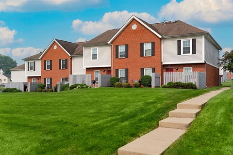 A red brick house with a white fence and a green lawn.