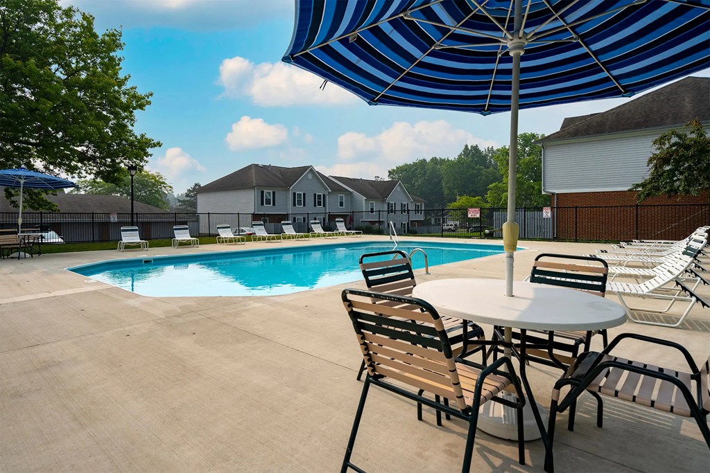A pool with chairs and an umbrella in the foreground.