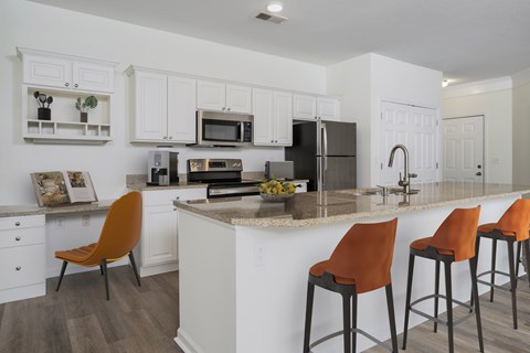 A kitchen with white cabinets and a counter with orange barstools.