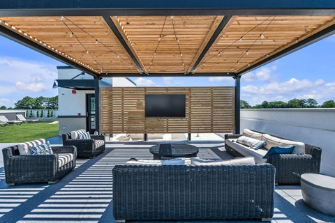 A patio with a television and furniture under a wooden roof.