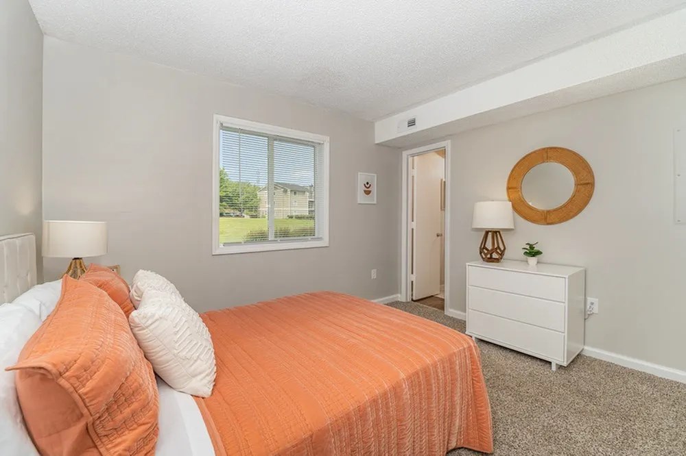 a bedroom with an orange bed and a window at Village 1373, Greensboro