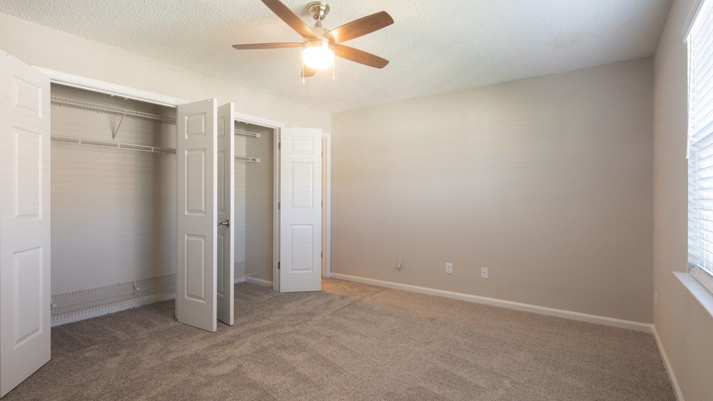 an empty living room with a ceiling fan and a closet