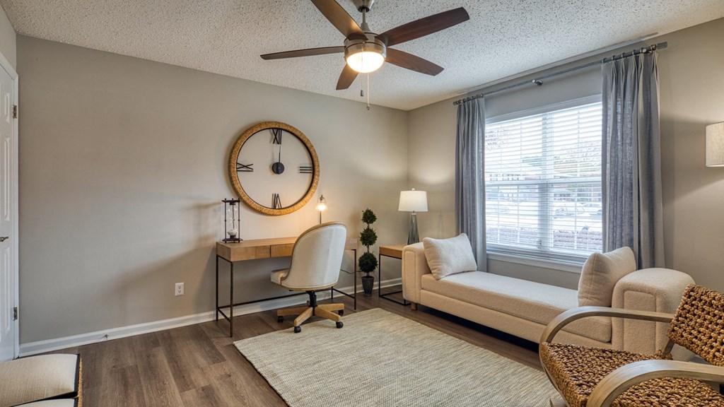 A room with a ceiling fan, a desk with a chair, and a window with curtains.