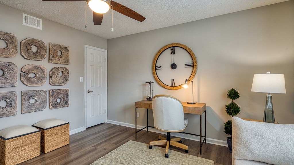 A room with a white chair, a desk with a lamp, a clock, and a wall with circular artworks.