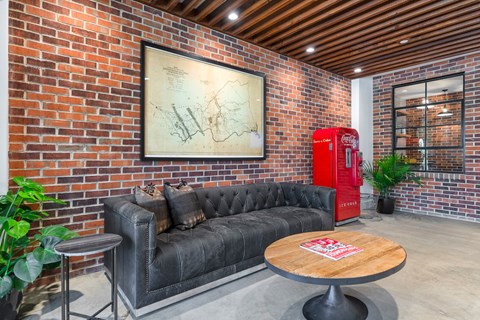 A room with a black couch, a wooden table, and a red Coca-Cola fridge.