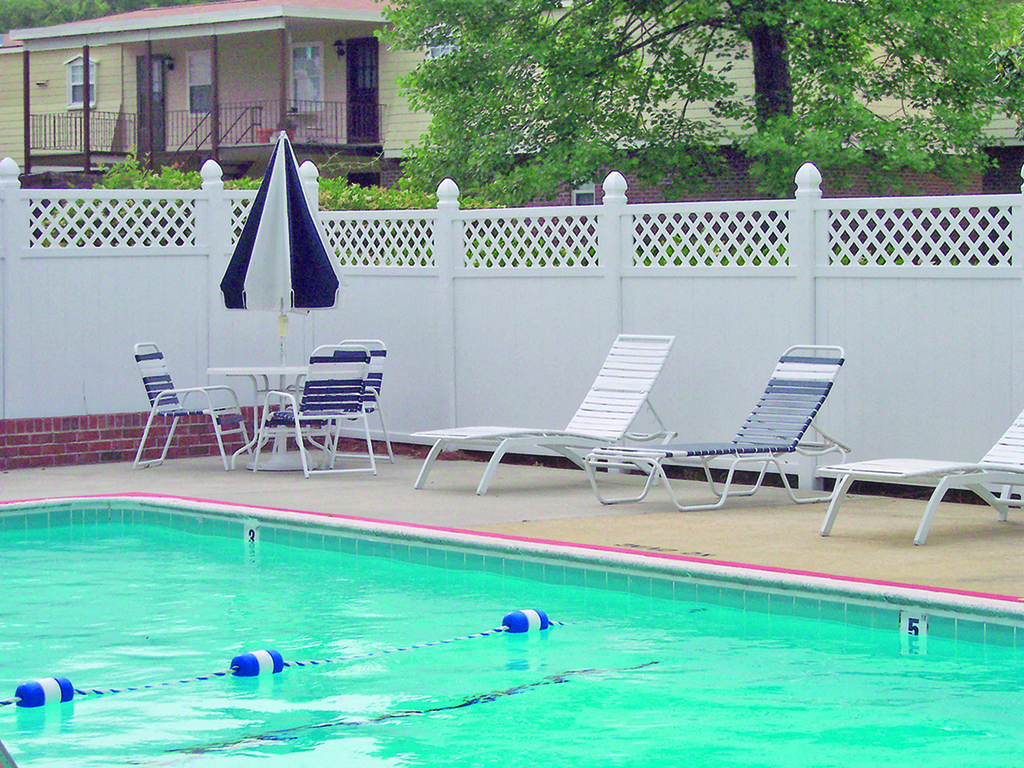 A pool with a white fence and chairs around it.