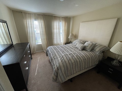 A bedroom with a bed, nightstand, and window with curtains.