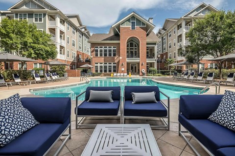 A pool area with blue couches and a brick building in the background.