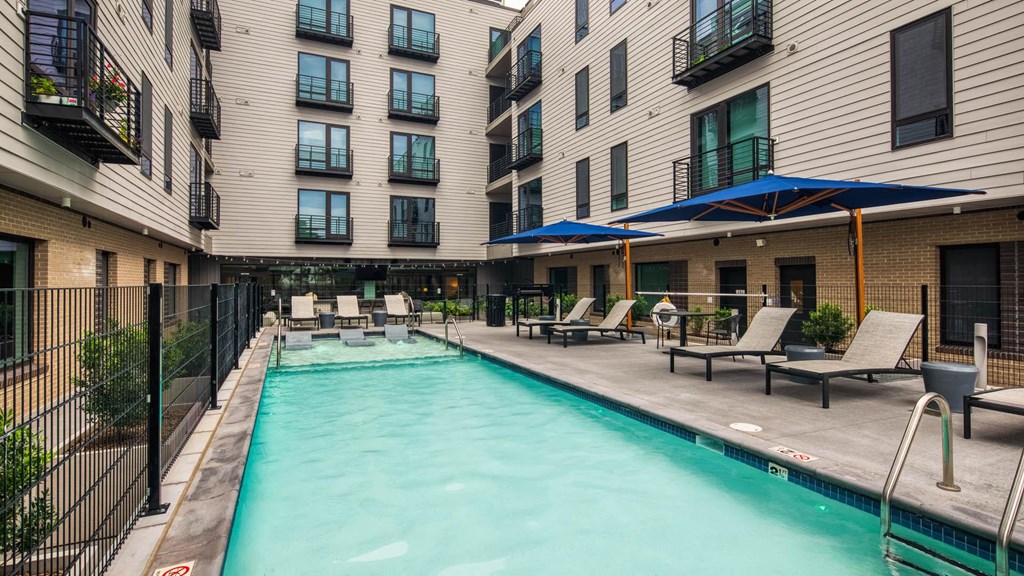 a swimming pool with chairs and umbrellas in front of an apartment building