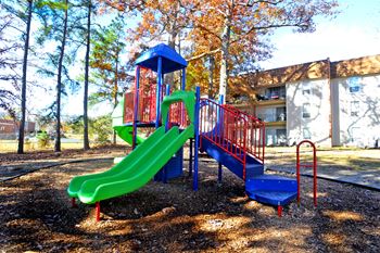 a playground with a green and red slide and a blue and red swing set