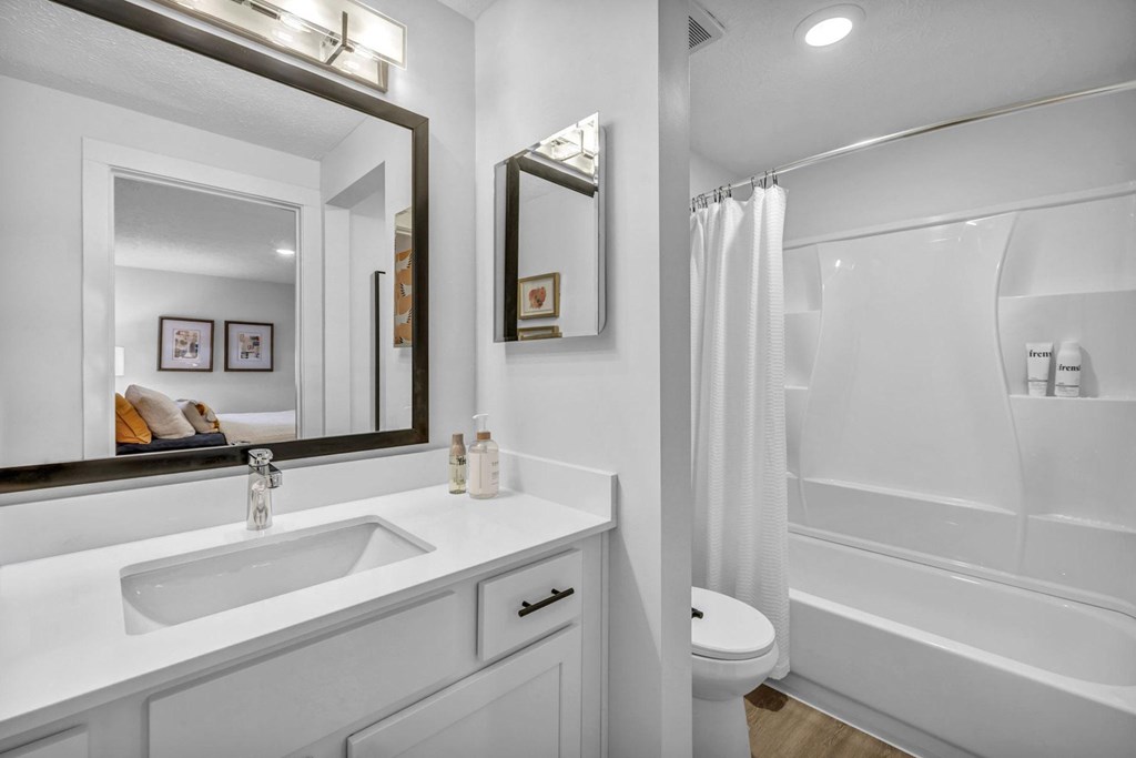 A white bathroom with a sink, mirror, and bathtub.