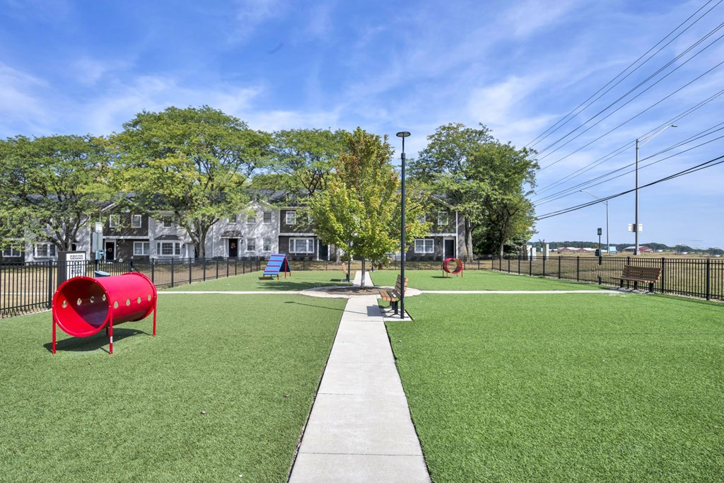 A playground with a red tunnel and a green lawn.