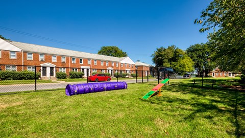 A playground with a purple slide and a red car parked in front of a brick building.