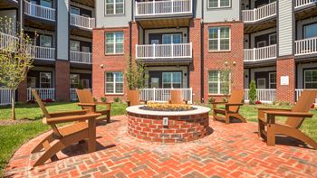 A fire pit sits in the middle of a brick patio surrounded by wooden chairs.