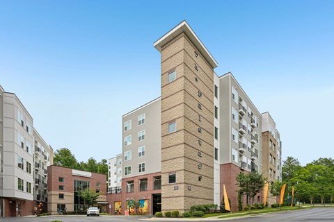A tall brick building with a clock tower on the top is surrounded by other buildings.