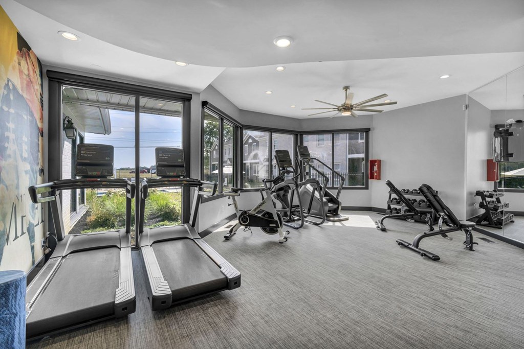 A spacious gym with treadmills, exercise bikes, and a fan.
