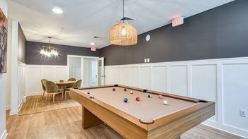 A pool table with a green chair and a brown table in the background.