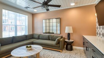 A living room with a grey sofa, a round table with a bowl on it, a lamp, and a ceiling fan.