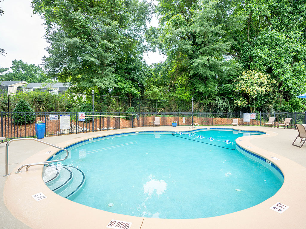 A large outdoor swimming pool surrounded by a fence and trees.